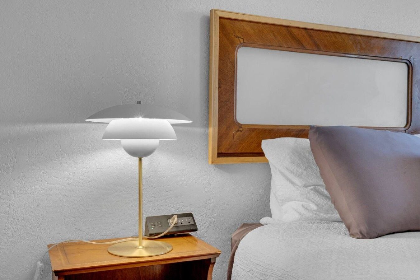 Un comodino con una lampada, una ciabatta multipresa e uno specchio fissato alla parete.