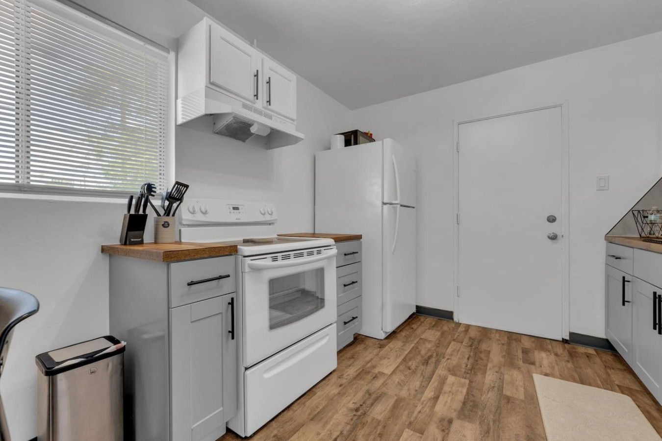 Een moderne keuken met witte kastjes, een ingebouwde oven, een koelkast en een houten aanrecht.