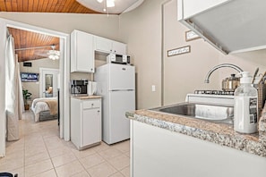 Una cocina compacta con muebles blancos, un microondas, una cafetera y un fregadero.