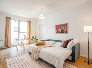 A modern bedroom with a bed, bedside table, and a window with curtains. - Emora | The Artful Prague Retreat (Prague)