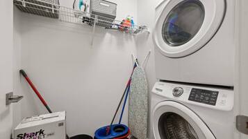 A laundry room with a washing machine, a mopping bucket, a mop, and a box labeled 'Shark Cortez PRO'.