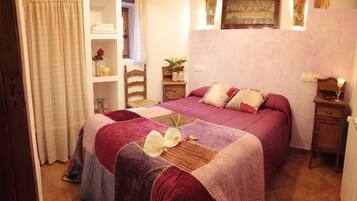 Un dormitorio con una cama grande, cabecera de madera, mesita de noche, estante con adornos y ventana con cortinas.