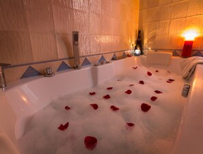 A bathtub filled with bubbles and rose petals, a bottle of champagne, and a candle on a side table. - Romantic Retreat With Pool and Jacuzzi (Laroya)