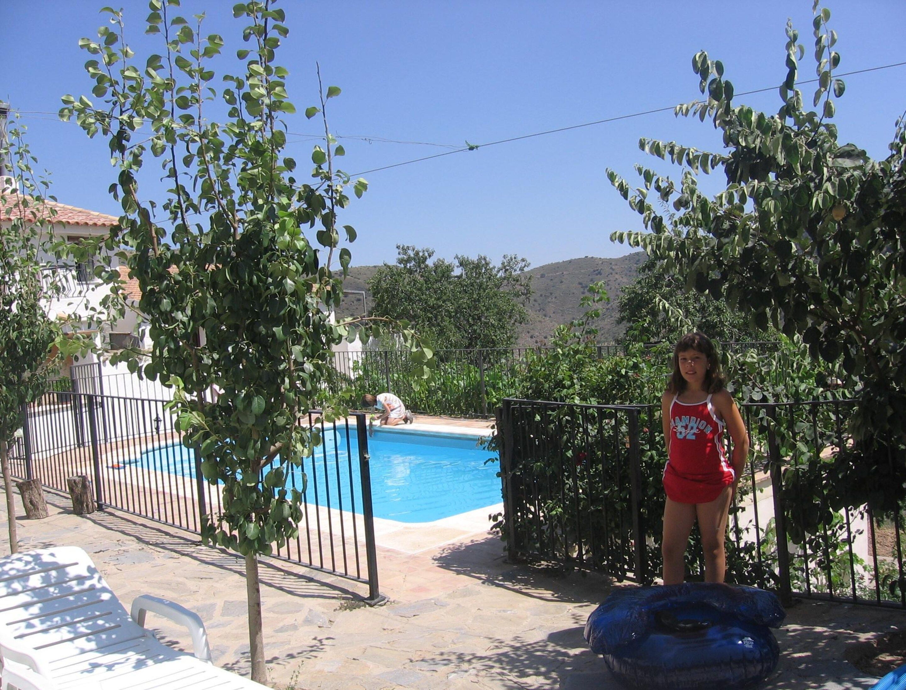 Una piscina con área cercada, una silla de descanso y una persona junto a la piscina.