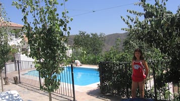 Una piscina con área cercada, una silla de descanso y una persona junto a la piscina.