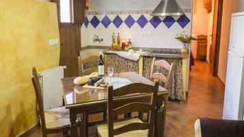 Comedor con una mesa lista para cuatro, sillas, un radiador, una cocina al fondo con un salpicadero de azulejos y un extintor de incendios montado en la pared.