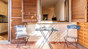 Une pièce avec un mur lambrissé en bois, une fenêtre donnant sur un paysage agréable, deux chaises en métal, une petite table sur laquelle sont posés quelques objets et un sol carrelé.