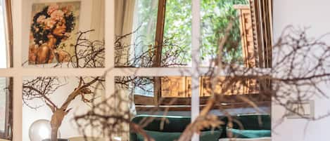 A room with a window, a painting, a vase, and a plant.