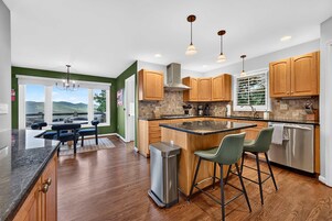 A modern kitchen with wooden cabinets, a stainless steel refrigerator, and a bar area with stools.
