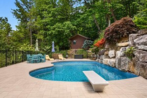 A swimming pool with a stone wall and a small cabin in the background.