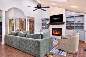 A modern living room with a grey sofa, a beige armchair, a fireplace, and a television mounted on the wall.