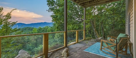 Un espacio al aire libre techado con suelo de piedra, mobiliario de madera y vista a un paisaje boscoso.