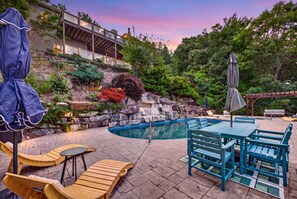 Un patio trasero con piscina, muebles de exterior y un muro de contención de piedra con plantas.