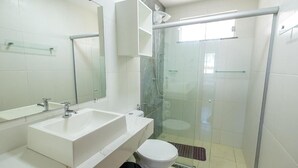Casa de banho com lavatório branco, espelho e cabine de duche em vidro.