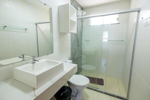 Un baño con lavamanos blanco, espejo y cabina de ducha con mampara de vidrio.