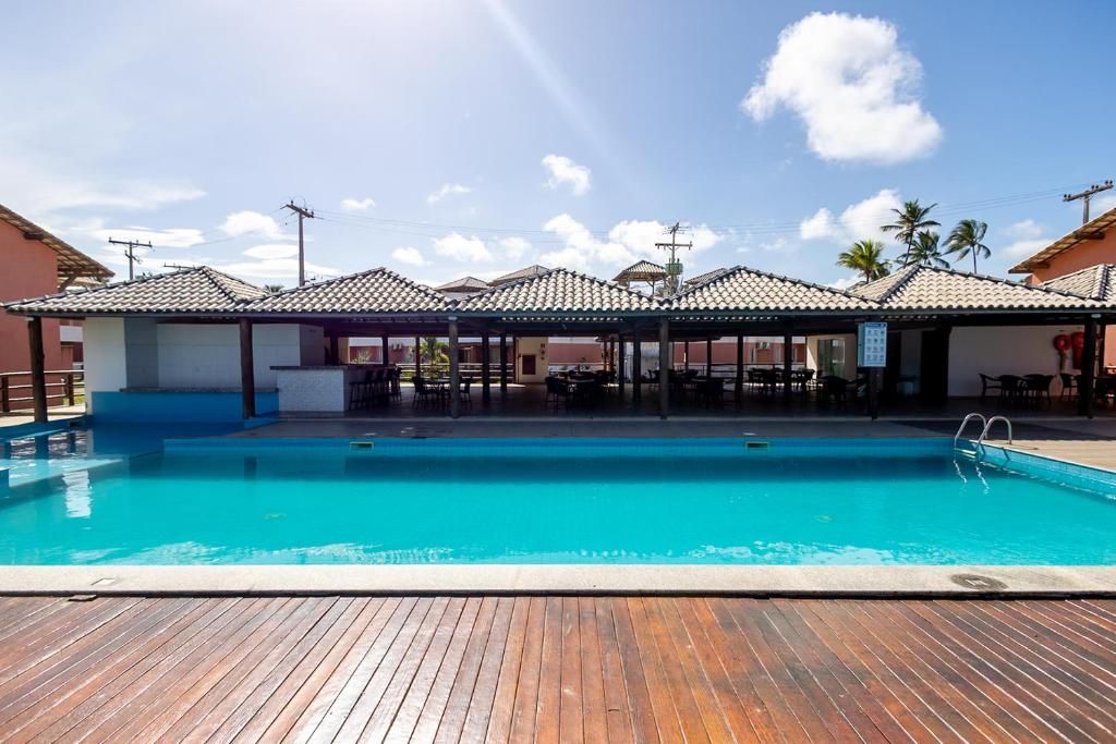 A swimming pool with a wooden deck, surrounded by covered seating areas and a clear sky.