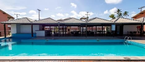 En swimmingpool med ett trädäck, omgiven av överbyggda sittplatser och en klar himmel.