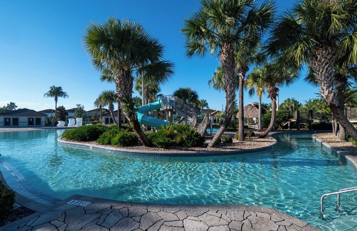 A swimming pool with a slide, surrounded by palm trees and a clear blue sky.