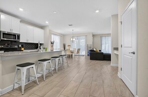 A modern kitchen with white cabinets, a black countertop, and two white bar stools. - Low-Tox Theme Park Retreat • 2 Private Theaters (Four Corners)