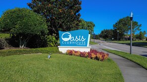 Een bordje voor Oasis Clubhouse bij Champions Gate, met een heldere lucht en groen in de achtergrond.