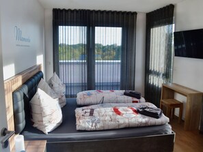 Ein modernes Hotelzimmer mit Bett, kleinem Tisch, Fernseher und einem Fenster mit Vorhängen.