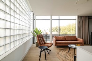 Ein modernes Wohnzimmer mit großem Fenster, einem braunen Ledersofa, einem kleinen schwarzen Tisch und einem Blumentopf.