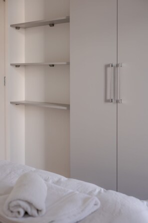 A bedroom with a bed, a wardrobe with shelves, and a towel on the bed.