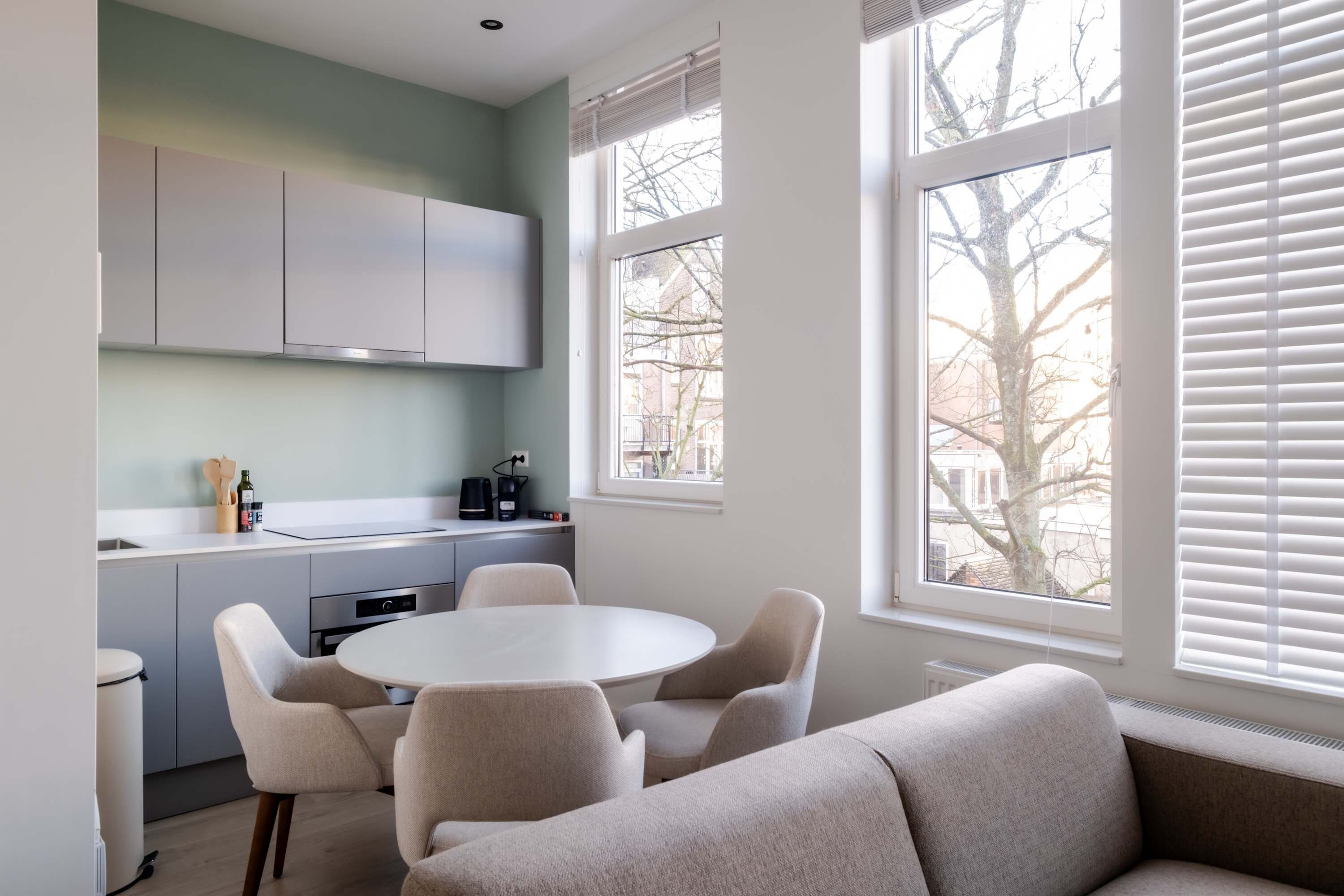 Une cuisine moderne avec des meubles blancs, une table à manger ronde et des chaises de couleur beige.