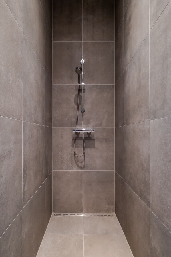 A shower area with a handheld showerhead and a wall-mounted faucet.