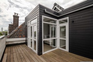 A rooftop terrace with a wooden deck, a black exterior wall, and a glass door leading to a balcony. - Grand apt w 2 Private Terraces and Free Parking (Rotterdam)