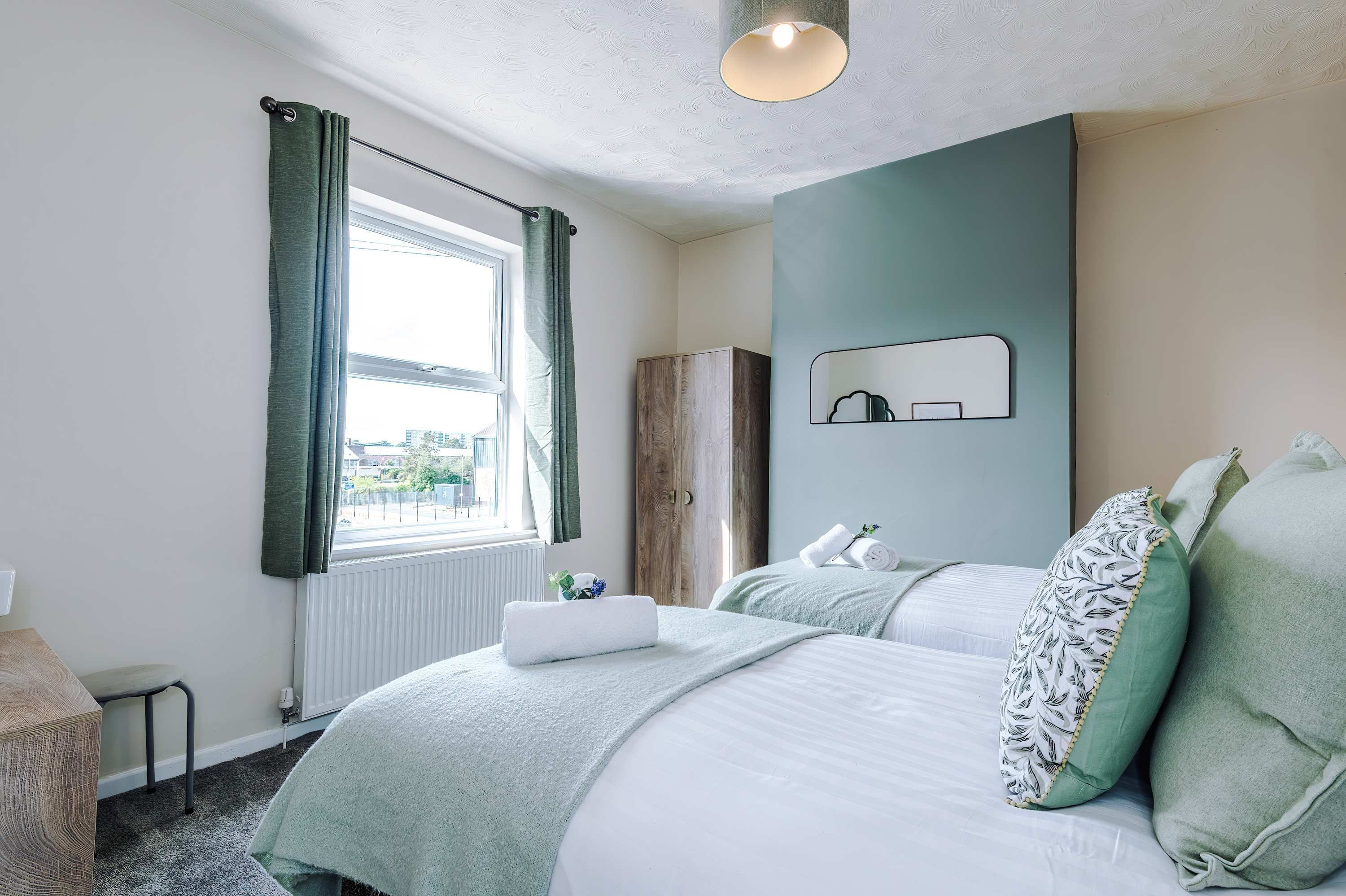 Een slaapkamer met een bed, een raam met gordijnen, een radiator, een spiegel en een nachtkastje.