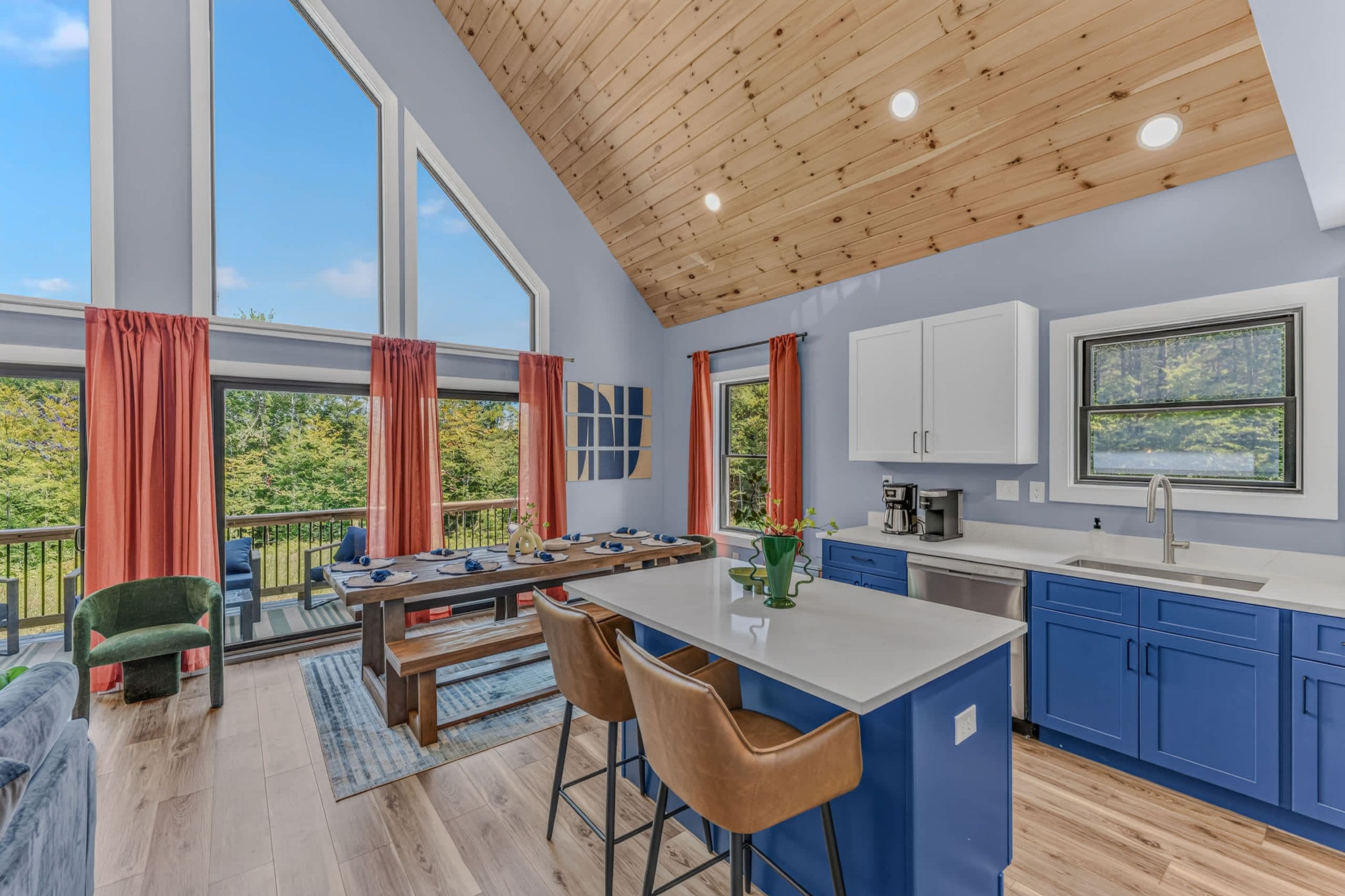 A modern kitchen with blue cabinets, a wooden ceiling, and large windows.