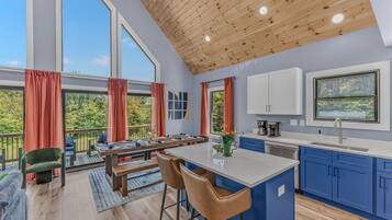 A modern kitchen with blue cabinets, a wooden ceiling, and large windows.