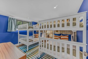 Habitación con literas para niños, suelo a cuadros, ventana con cortinas y una mesa.