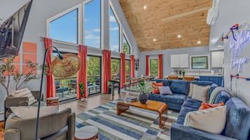 A spacious living area with large windows, a wooden ceiling, and a modern kitchen in the background.