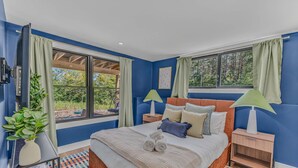 Een slaapkamer met een groot bed, twee nachtkastjes, een raam met gordijnen en uitzicht op groen.