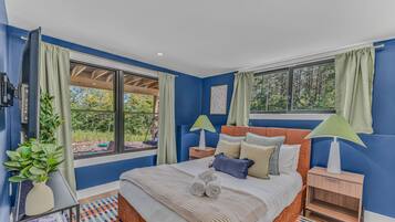 A bedroom with a large bed, two bedside tables, a window with curtains, and a view of greenery outside.