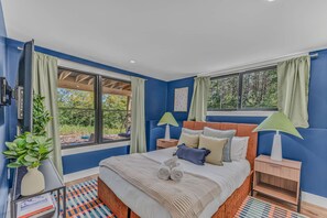 A bedroom with a large bed, two bedside tables, a window with curtains, and a view of greenery outside. - Sauna Hot Tub Game Room Theater Firepit (Bethel)