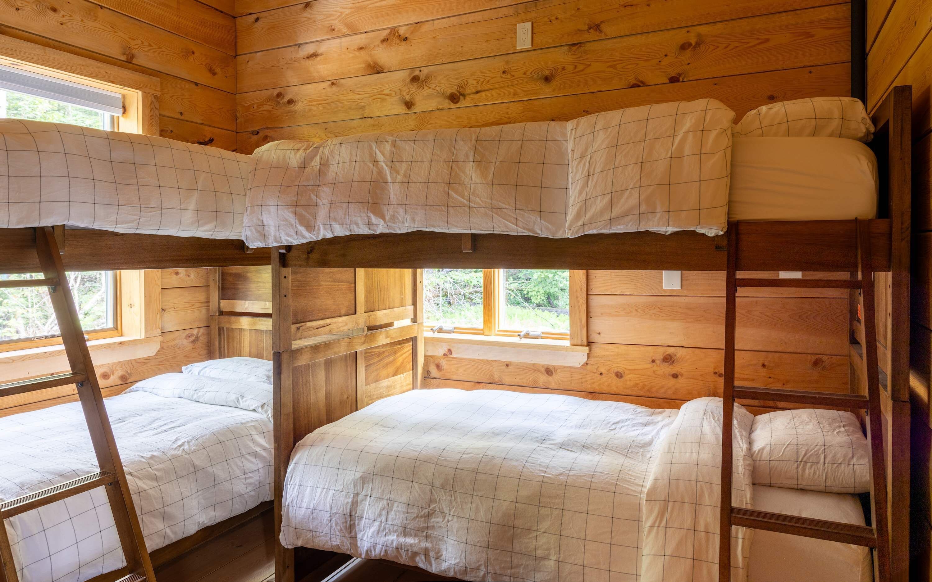 A cabin with a bunk bed arrangement, wooden walls, and a window providing natural light.