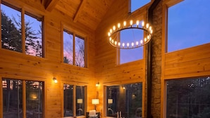 Interior acogedor de una cabaña con chimenea, muebles de madera y ventanas amplias.