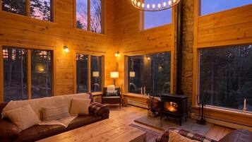 Interior acogedor de una cabaña con chimenea, muebles de madera y ventanas amplias.