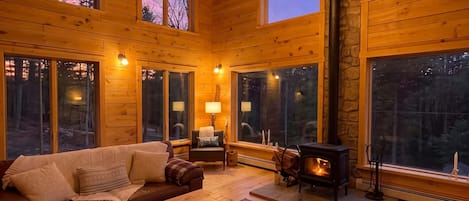A cozy cabin interior with a fireplace, wooden furniture, and large windows.