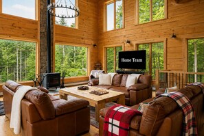 A spacious living room with a fireplace, leather sofas, a coffee table, and a television labeled 'Home Team.' - The Grafton Lodge Secluded Green Mountain Escape (Grafton)