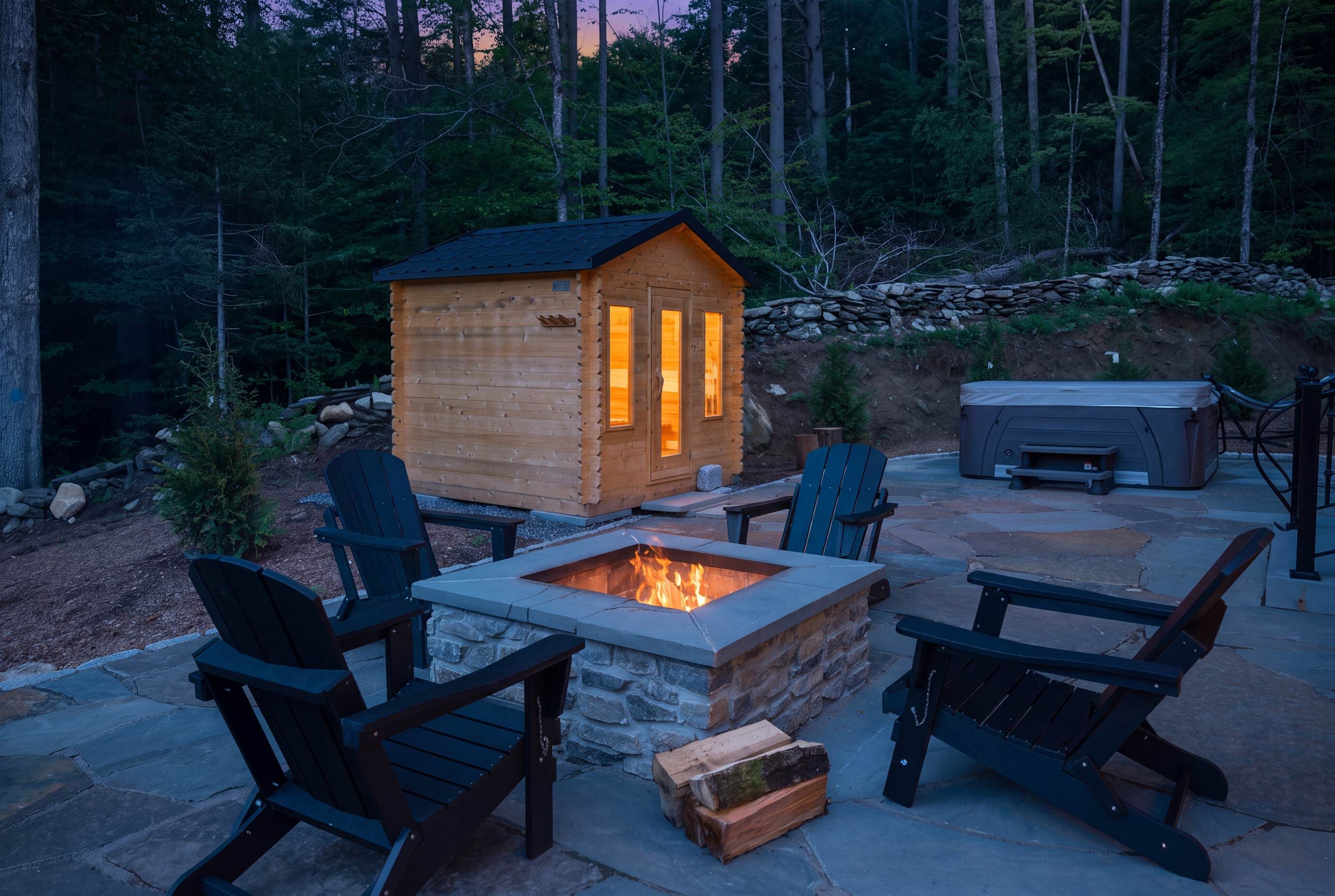 A wooden cabin with a fire pit in the center, surrounded by Adirondack chairs and a stone fire table.
