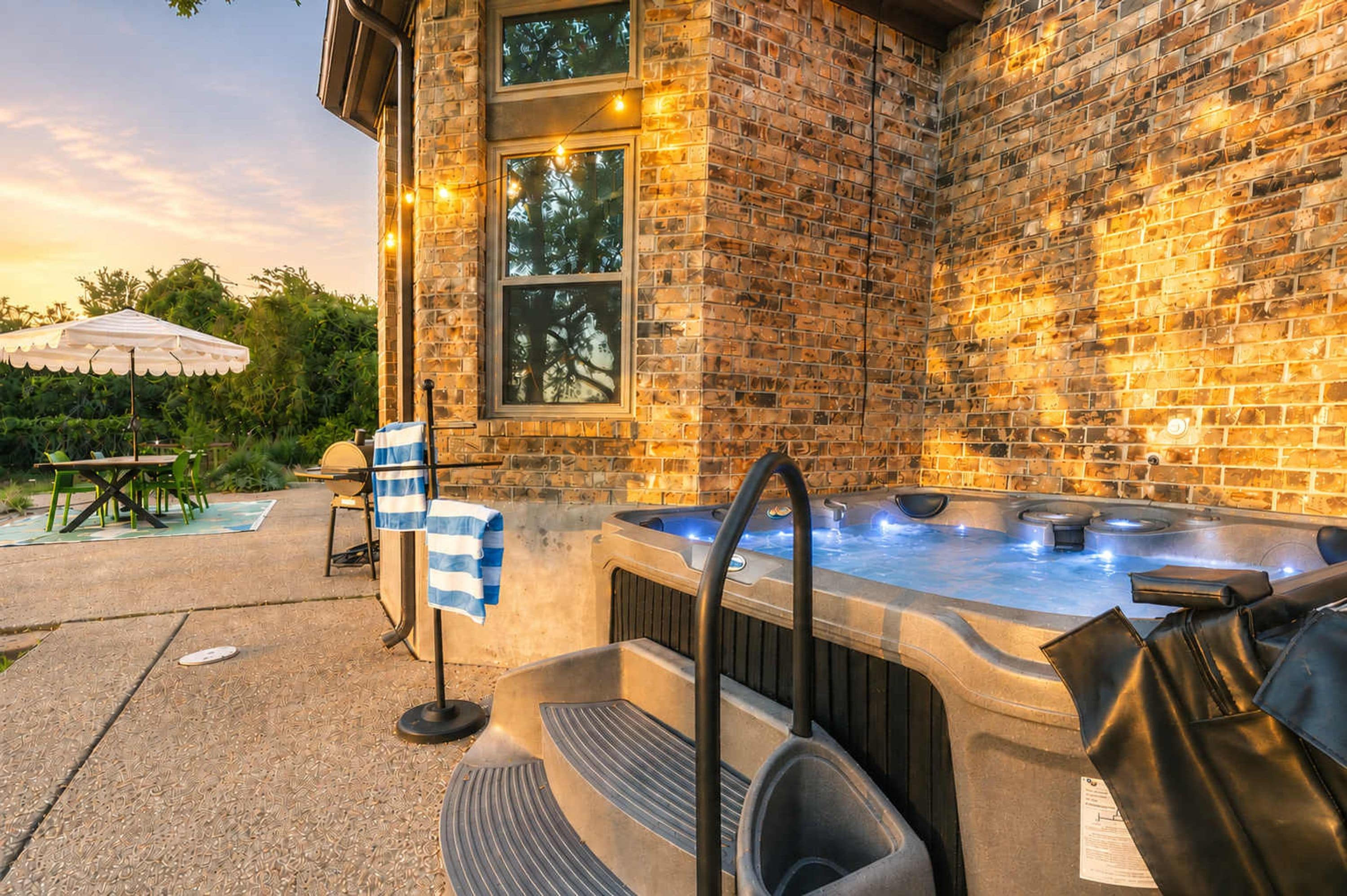 An outdoor hot tub area with a brick wall, a covered seating area, and a pool in the background.