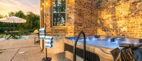 An outdoor hot tub area with a brick wall, a covered seating area, and a pool in the background.