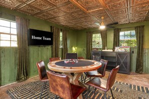 A room with a round table, leather chairs, a television labeled 'Home Team,' and a bar area with Monopoly games. - The Canyon Social Pool Hot Tub Sport Court (Dripping Springs)