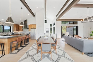 A modern kitchen with a central island, bar seating, and a dining area with a large table. - Bear Scratch Mountain Views Modern Luxury (Crested Butte)