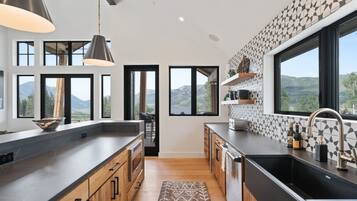 A modern kitchen with a large island, black countertops, wooden cabinets, and a view of the mountains through large windows.