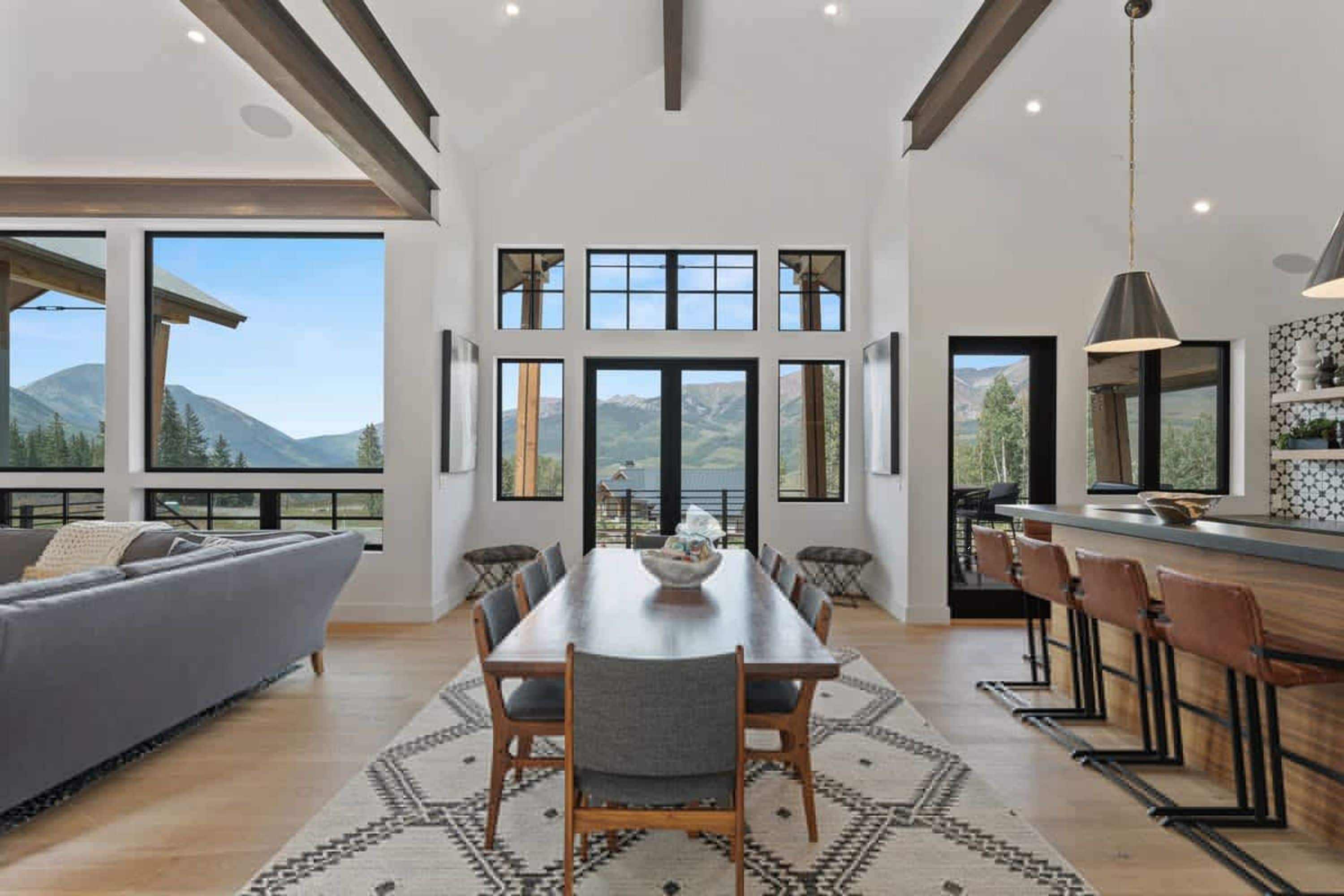 A modern kitchen with a dining area, large windows, and a view of mountains.
